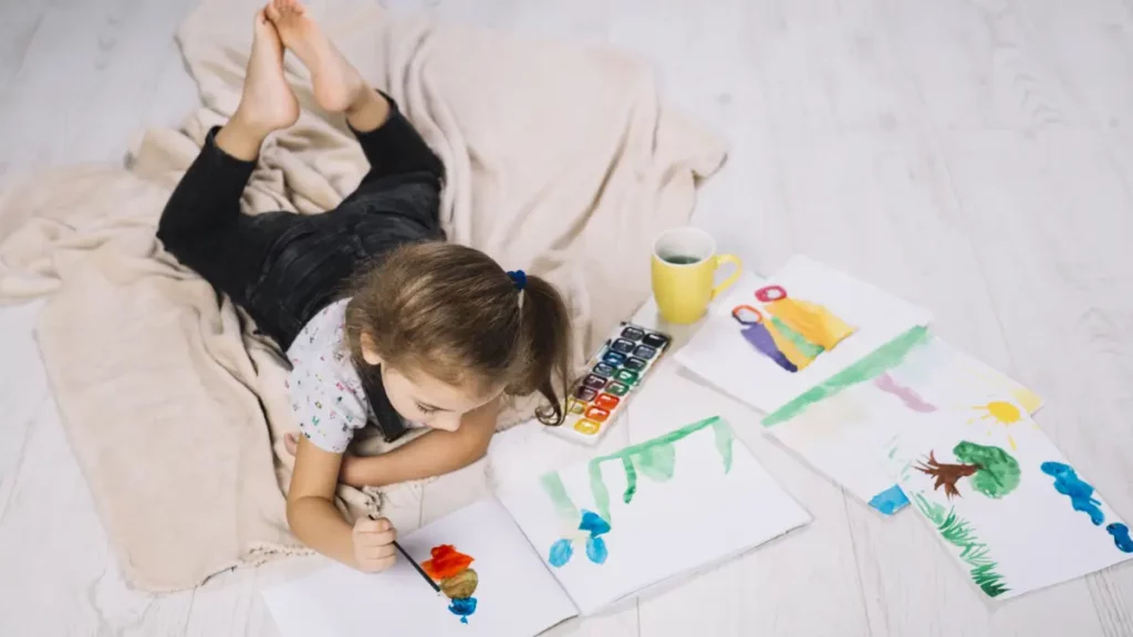 Dziewczynka maluje obrazy na podłodze ciesząc sie rysując