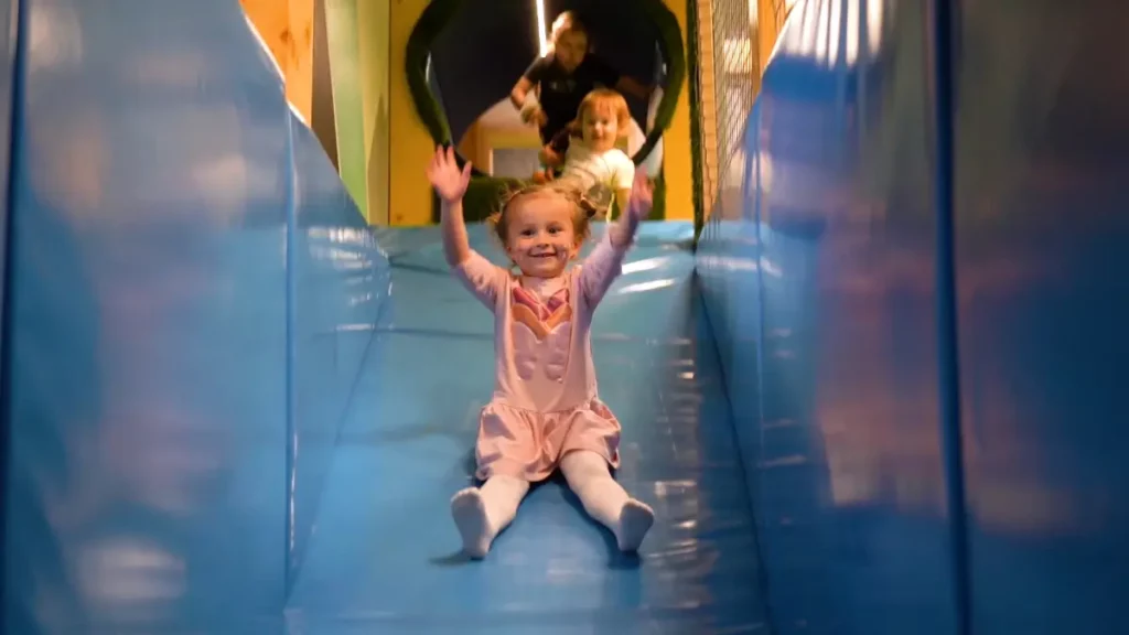 Rozwój pewności siebie i socjalizacji w górskiej sali zabaw, dziecko zjeżdża na zjeżdżalni na sali zabaw